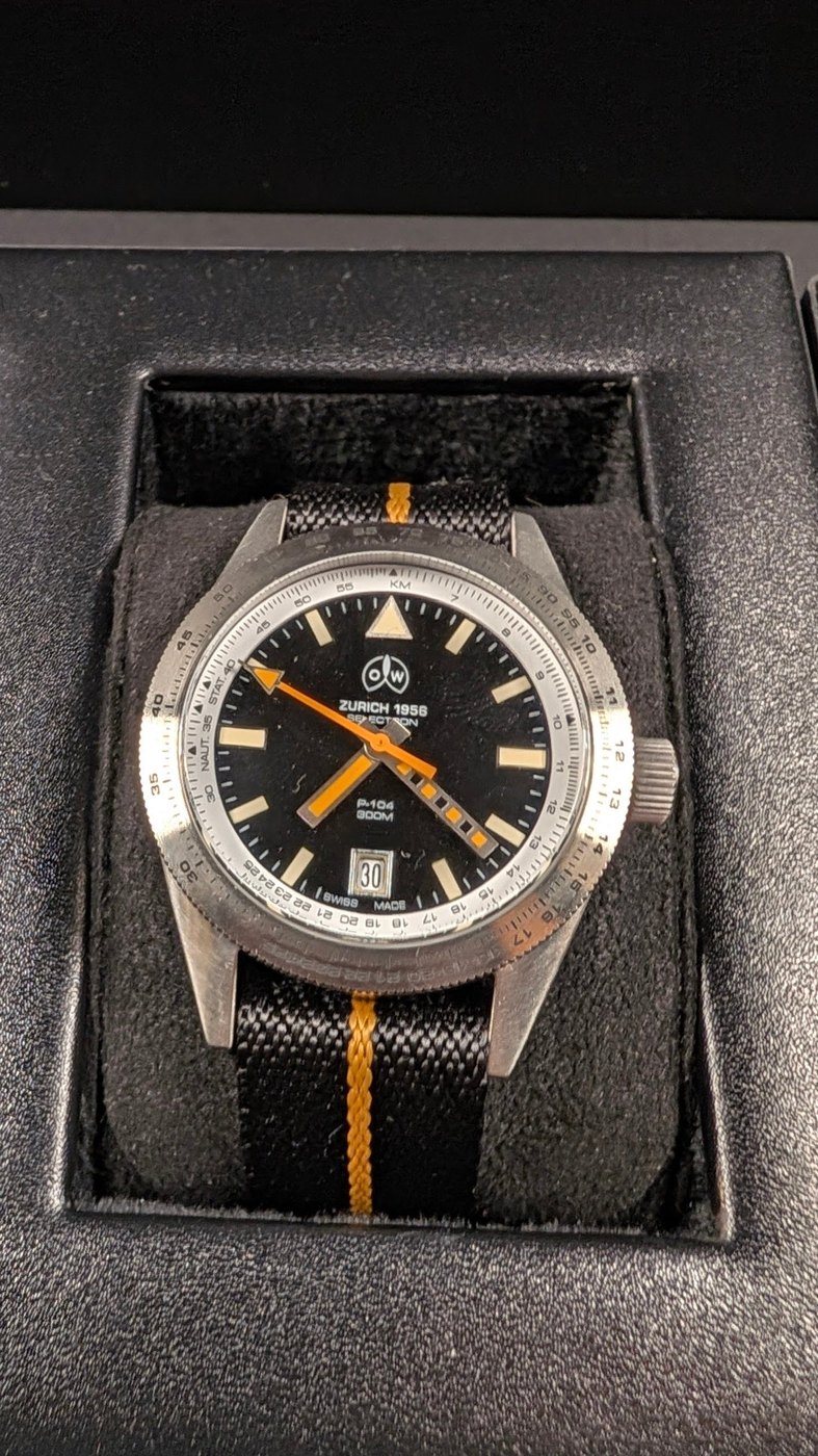 Ollech & Wajs P-104 watch with a black dial and orange hands, photographed inside Model D.