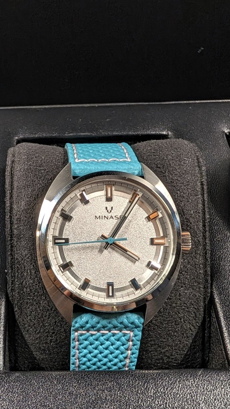 A watch with a silver dial and turquoise strap, photographed inside Model D.